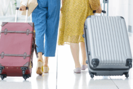 Duas pessoas caminhando lado a lado em um aeroporto, cada uma puxando sua bagagem de mão sobre o piso brilhante do terminal.