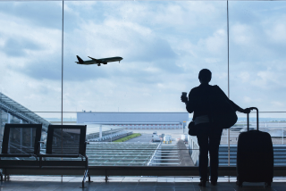 Viajante com mala observando um avião decolando através da janela de um aeroporto.