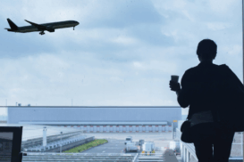 Viajante com mala observando um avião decolando através da janela de um aeroporto.