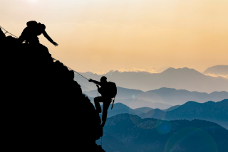 Sombra de duas pessoas escalando uma montanha. A primeira está mais acima e estende a mão para ajudar a segunda.