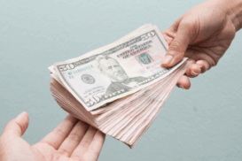 Duas mãos aparecem em destaque, uma entregando e outra recebendo um maço de notas de dólar americano