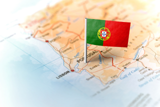 Pequeno alfinete com a bandeira de Portugal fincado em um mapa que destaca o território português, com a cidade de Lisboa visível em destaque.